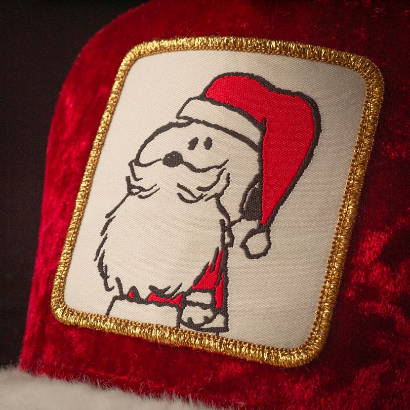 Close up of a woven patch of Snoopy from the Peanuts wearing a Santa suit attached to the crown.