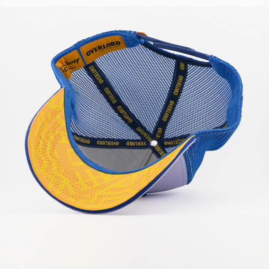 Underside of the Zazu from Disney's The Lion King retro trucker cap showing a yellow patterned brim with blue border, blue mesh crown, Disney tag, and yellow Overlord branded taping with black text.